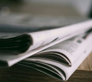 Stack of folded newspapers on a wooden table with a focus on printed pages.